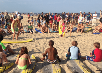 a group observing a man standing next to surfboard